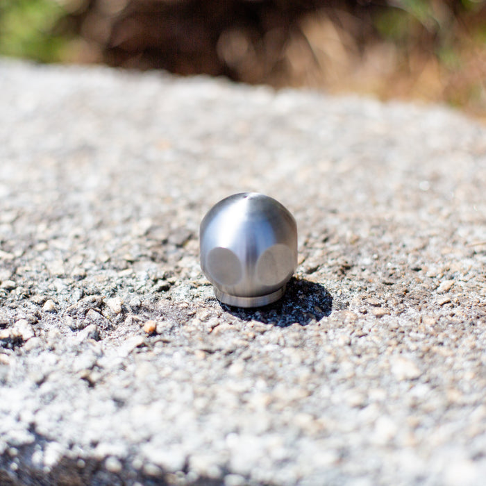 Stainless steel ball jet sewer jetter nozzle on asphalt surface, high-pressure drain cleaning nozzle for hydro jetting, durable multi-port jet nozzle for clearing pipes, grease, and debris in plumbing and sewer lines