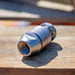 ENZ Bulldog rotating sewer jetting nozzle on a wooden surface, featuring a stainless steel body with precision‑machined jets and threaded inlet; built with an oil‑free braking system for controlled slow rotation, compatible with fresh or recycled water, and engineered for cutting grease, roots, and heavy pipeline deposits with 6-inch rear jets and 1-inch forward jet performance; optional 90‑degree descaling head available for removing tough scale from pipe walls.