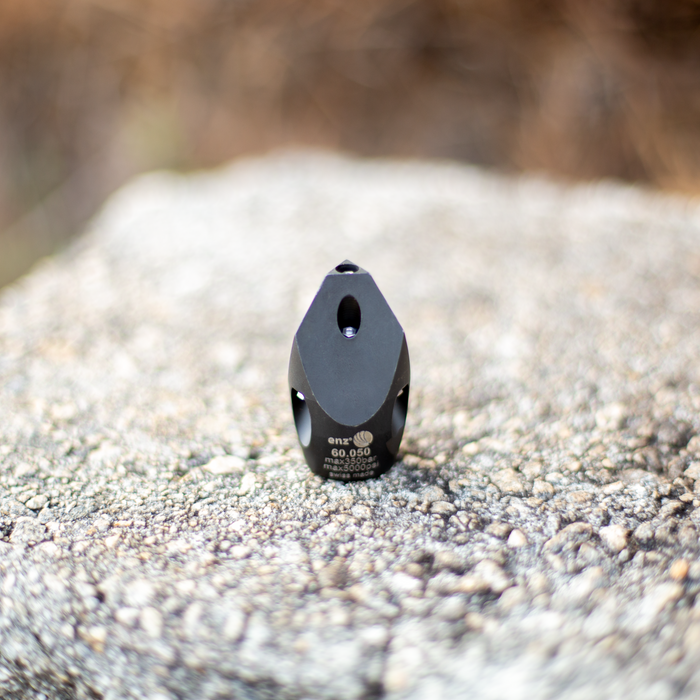 Enz 60.050 high‑pressure sewer jetting nozzle shown in close‑up on a textured outdoor surface, featuring a black Swiss‑made stainless steel body with multiple angled jet ports for precision cutting and cleaning. Industrial chisel‑style sewer nozzle rated to 350 bar / 5000 psi, engineered for forward‑firing penetration jets and rear thrust jets to clear grease, light roots, and general pipe debris in professional drain and sewer maintenance.