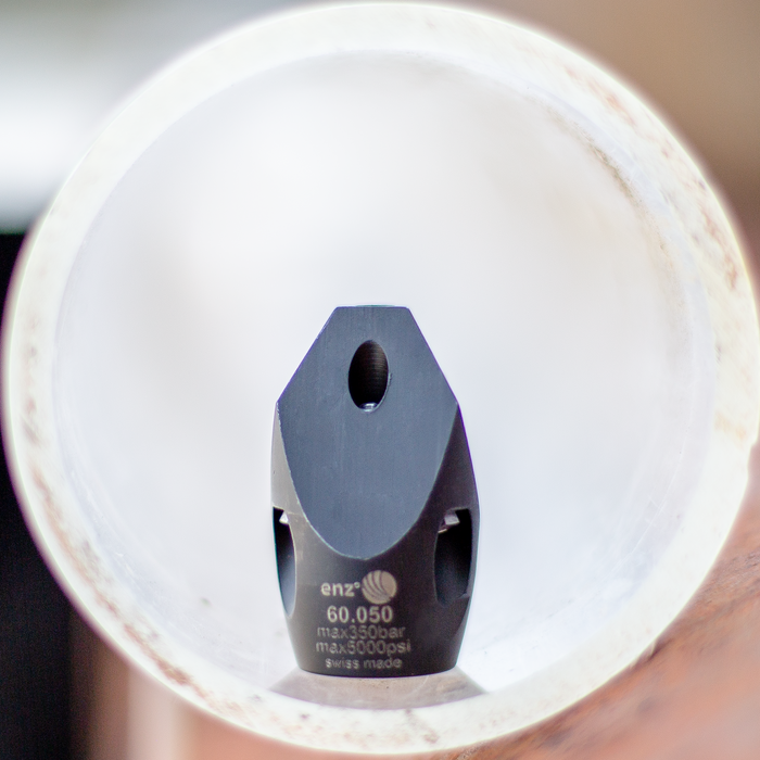 Enz 60.050 high‑pressure sewer jetting nozzle operating inside a pipe, shown in close‑up with multiple precision jet ports and a Swiss‑made stainless steel body rated to 350 bar / 5000 psi. Industrial chisel‑style sewer cleaning nozzle designed for forward‑cutting penetration jets and rear thrust jets to clear grease, light roots, and general pipe debris during professional drain and sewer maintenance.