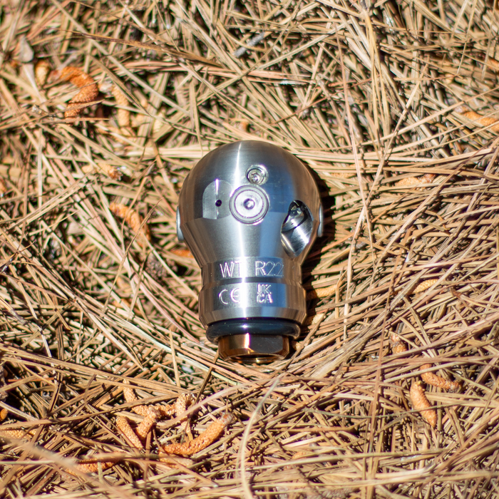 3/8-inch Warthog Mini SuperSpin WT sewer jetting nozzle on pine needles, stainless steel 4000 PSI 12 GPM rotating drain cleaning nozzle with 2 rear jets and 1 forward jet for grease, hair roots, and 3–6 inch pipe cleaning; controlled‑rotation Warthog WT nozzle for residential and food industry sewer maintenance.