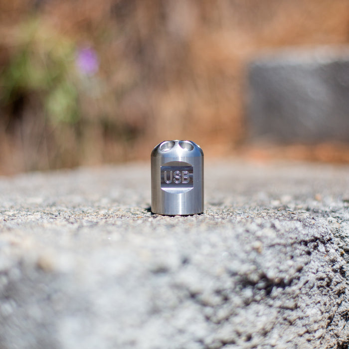 Stainless steel Digger Nozzle for sewer jetting, forward‑jet design with no rear jets to push debris and scale out of small pipes; manually pushed nozzle ideal for short runs under 100 feet during pipe‑lining prep, shown on a rough stone surface in natural outdoor light.