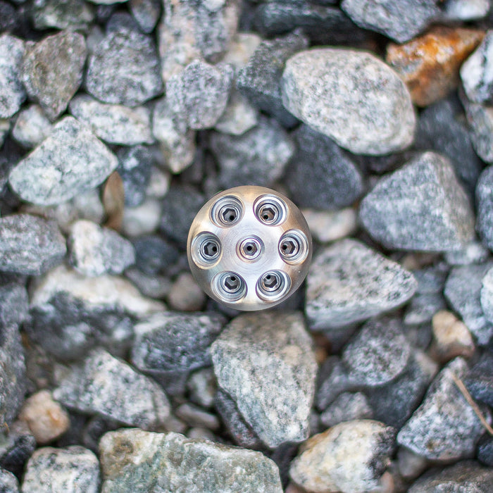 Stainless steel Digger Nozzle for sewer jetting, forward‑jet design with no rear jets to push debris and scale out of small pipes; manually pushed nozzle ideal for short runs under 100 feet during pipe‑lining prep, shown on rocky surface for product detail.