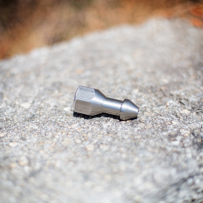 “SJ Penetrator 1/2-inch stainless steel sewer jetting nozzle on rough stone surface, close-up of precision‑machined forward jet and six rear jet ports engineered to break through hard blockages like packed debris or ice; high‑pressure 4018 jetter nozzle with adapters available for other hose sizes.