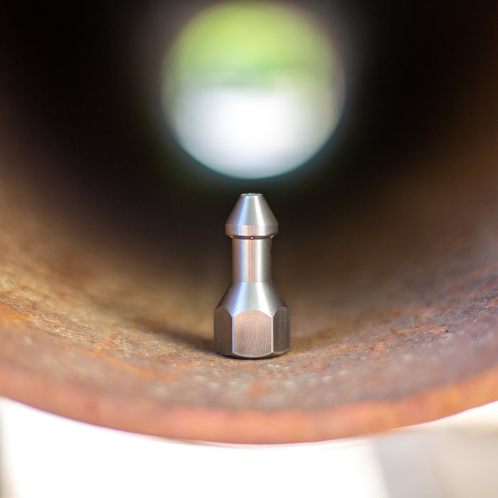 USJ Penetrator 1/2-inch stainless steel sewer jetting nozzle positioned inside a rusted pipe, close-up of precision-machined forward jet and six rear jet ports engineered to break through hard blockages like packed debris or ice; high‑pressure 4018 jetter nozzle with adapters available for other hose sizes.