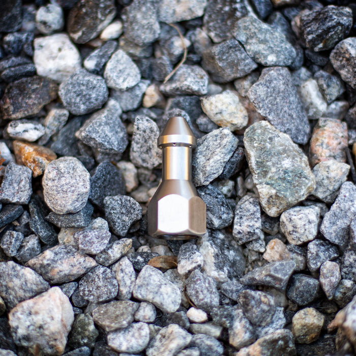 USJ Penetrator 1/2-inch stainless steel sewer jetting nozzle on gray stone surface, close-up of precision-machined forward jet and six rear jet ports engineered to cut through hard blockages like packed debris or ice; high‑pressure 4018 jetter nozzle with adapters available for other hose sizes.