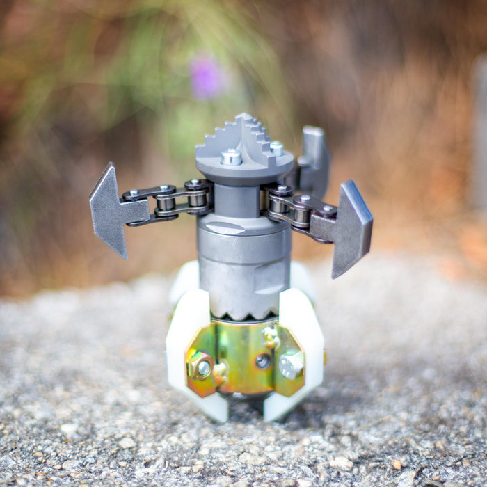 Close‑up of an ENZ Turbo Chain Scraper nozzle on a concrete surface, featuring a heavy‑duty toothed cutting head, black rotating chain arms with adjustable links, and white centralizing skids. Industrial sewer jetting tool engineered for clearing concrete, roots, and grease from 3–8 inch pipes, built for rugged conditions and compatible with jetting machines requiring at least 8 GPM.