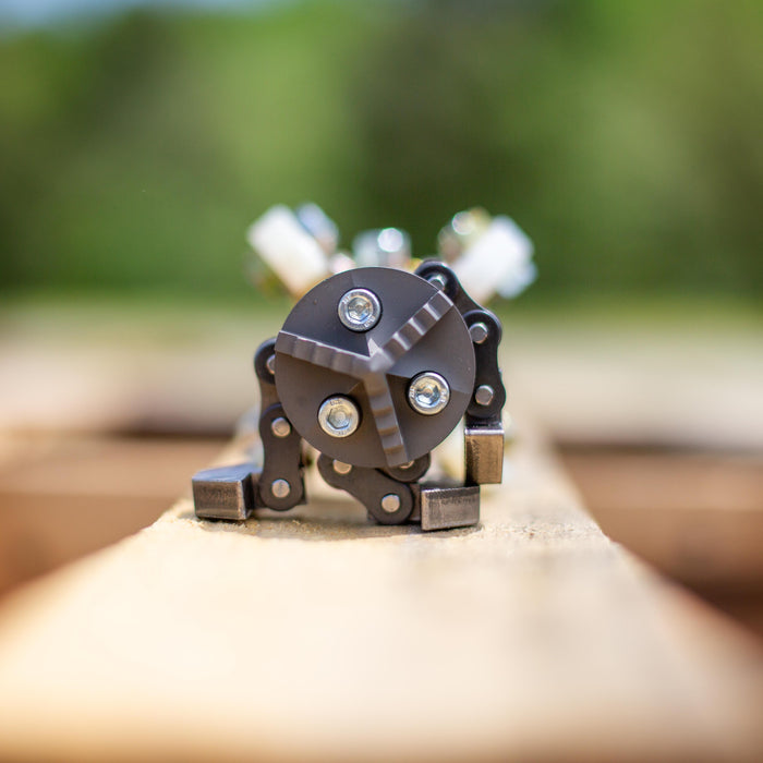 Close‑up of an ENZ Turbo Chain Scraper component on a wooden pallet, featuring a compact circular chain‑scraper head with heavy‑duty linkage arms and rugged mounting hardware. Industrial sewer jetting tool designed for clearing concrete, roots, and grease from 3–8 inch pipes, built for harsh conditions with adjustable chain lengths and centralizing skids for pipe protection.
